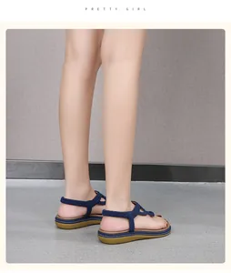 Detail view of navy blue bohemian braided sandals on a model standing on gray carpet.