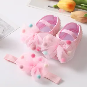 Close-up of pink baby shoes and headband set with colorful pom-poms on sheer bows.