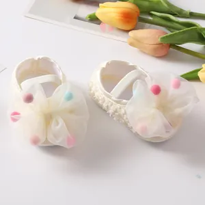 Close-up of white baby princess shoes with large mesh bow and colorful pom-poms