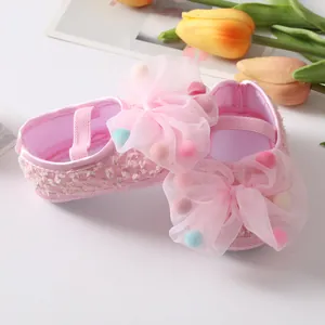 Close-up detail of pink baby princess shoes featuring large mesh bow and colorful pom-poms