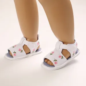 Gros plan de sandales blanches pour bébé avec broderie florale rose et velcro.