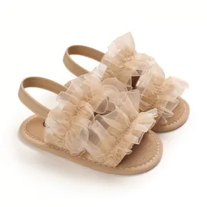 Detalle de sandalias para bebé con suela blanda, volantes de tul beige y tira elástica.