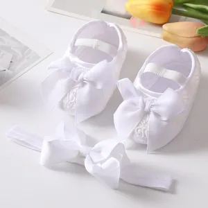 Detail view of white lace baby shoes with large bows and matching headband set.