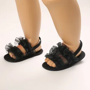 Primer plano de sandalias negras para bebé con volantes y correas de malla suave.
