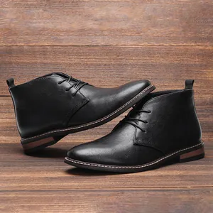 Detailopname van zwarte heren lederen desert boots op een rustieke houten wand.