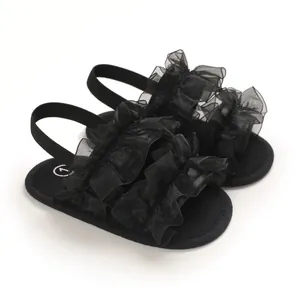 Elegantes sandalias negras para bebé con volantes, suelas blandas y tiras traseras elásticas.