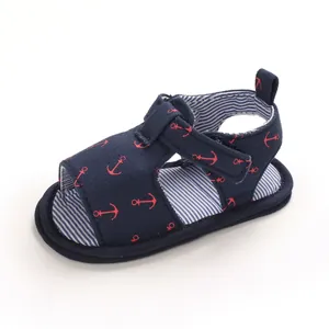Détail de sandale bébé bleu marine avec motifs ancres rouges et semelle rayée souple.