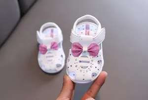 Nahaufnahme von weißen Baby-Prinzessin-Sandalen mit glitzernder rosa Schleife und Strasssteinen