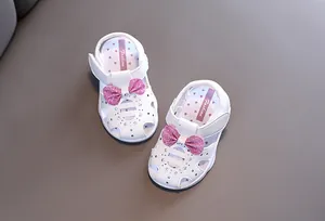 Nahaufnahme von weißen Sandalen für Kleinkinder mit rosa Glitzerschleifen und glänzenden Strass.