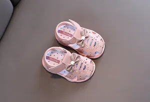 Detailansicht der glitzernden Schleife und Zierausschnitte an rosa Baby-Sandalen