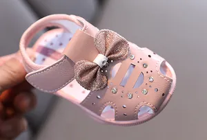 Nahaufnahme einer rosa Baby-Sandalette mit glitzernder Schleife und Strasssteinen