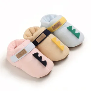 Chaussures souples pour bébé en coton avec motif queue de dinosaure en rose, jaune et bleu.
