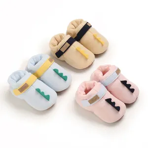 Vue rapprochée de chaussures pour bébé dinosaure aux couleurs bleu, beige et rose.