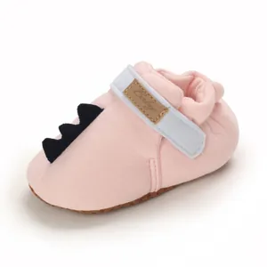 Gros plan d'une chaussure pour bébé rose avec un détail de queue de dinosaure noire