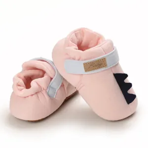 Chaussures de marche roses pour bébé avec détail de queue de dinosaure.