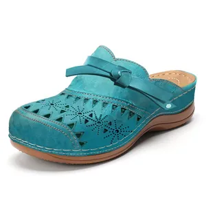Close-up detail of teal laser-cut leather mules with decorative bow and brown platform sole