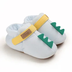 Gros plan de chaussures bébé bleu clair avec pointes de dinosaure et bride jaune.