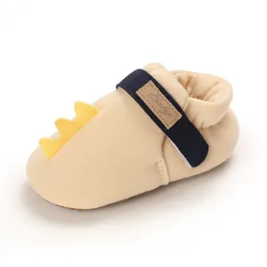 Détail d'une chaussure de bébé crème avec crête de dinosaure jaune et bride bleu marine