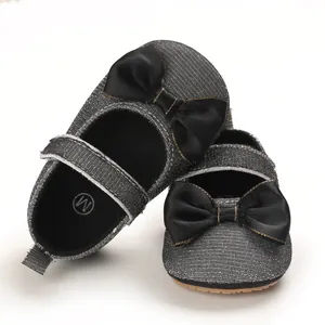 Detailaufnahme grauer Glitzer-Babyschuhe mit schwarzer Schleife und rutschfester Sohle.