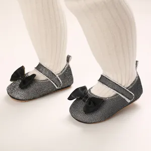 Detailaufnahme von silbernen Glitzer-Babyschuhen mit schwarzer Schleife und Klettverschluss
