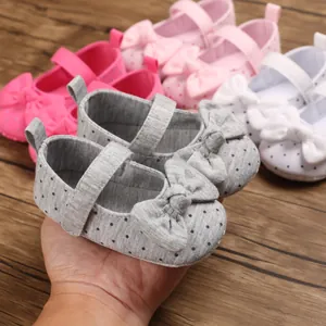 Close-up of grey polka dot baby girl shoes with bow and soft sole in hand.