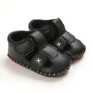Detailed macro view of black leather infant sandals with white X-stitching and red soles