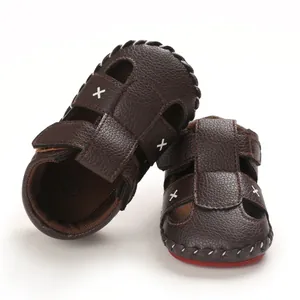 Detailed view of brown baby soft-sole sandals with cross patterns and red non-slip base