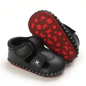 Detail view of the soft black leather material and red non-slip soles of infant sandals