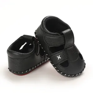 Close-up of black leather baby walking sandals with white X embroidery and red sole.
