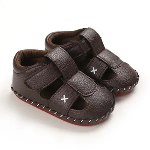 Close-up detail of brown baby sandals with soft soles and white 'X' embroidery.