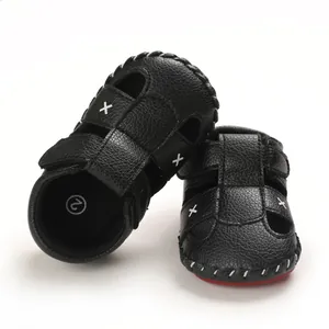 Detailed view of black infant walker sandals with white cross stitching and soft red soles