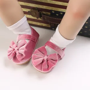 Close-up of pink velvet baby walker shoes with large decorative bows on soft soles