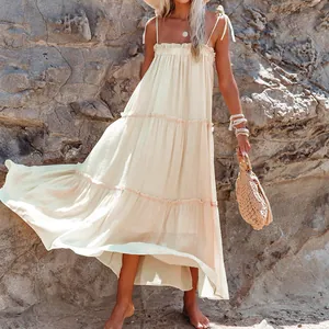 Tiered cream maxi dress with shoulder ties and ruffle detail on rocky beach background
