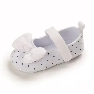 Side view of white polka dot baby girl princess shoes with a large white bow detail