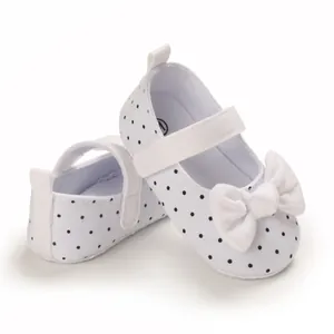 Close-up of white baby girl shoes featuring a black polka dot pattern and a white bow.