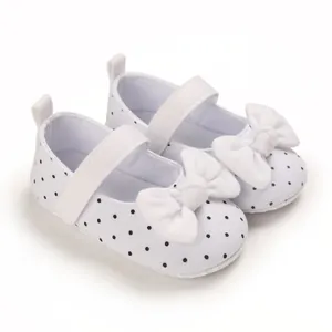 Detailed view of white baby girl walker shoes with black polka dots and a white bow.