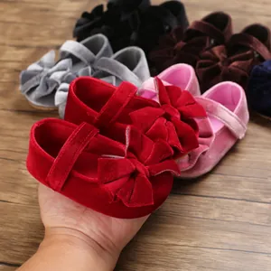 Hand holding a soft red velvet baby girl shoe with a large decorative bow ornament