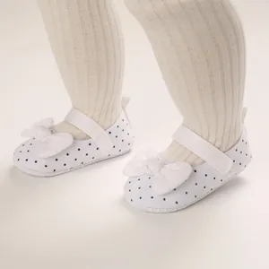 Close-up of white polka dot baby girl shoes with large bow and soft sole detail