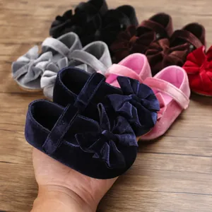 Close-up of velvet baby girl bow shoes in various colors on wooden surface.
