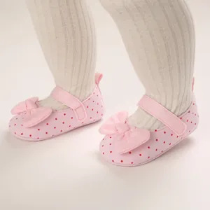 Close-up of pink polka dot baby princess shoes with bow and soft sole detail.