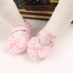 Close-up of pink polka dot baby princess shoes with bow on white ribbed leggings.