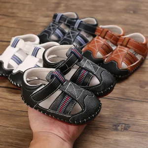 Detalle de sandalias negras suaves para bebés con cierres de velcro sostenidas en la mano.