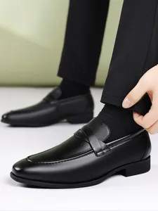 Close-up of black leather loafers with stitched details on a model wearing black trousers.