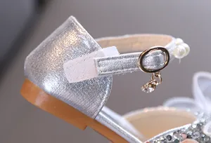 Detalle de zapatos de princesa plateados para niñas con correa de perlas y colgante
