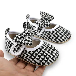 Close-up of baby girl walking shoes featuring black and white houndstooth pattern and bow