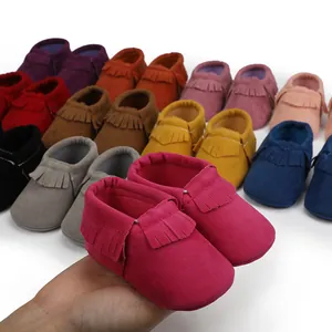 Nahaufnahme von pinkfarbenen Baby-Mokassins mit Fransen und bunten Schuhen im Hintergrund
