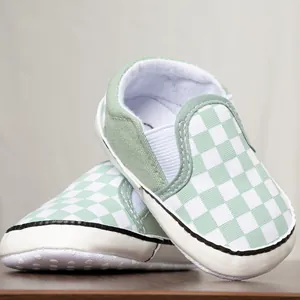 Primo piano di scarpe primi passi per neonati a scacchi verde salvia e bianco, suola morbida