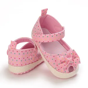 Gedetailleerd beeld van roze baby sandalen met stippen, zachte zolen en schattige strikjes.
