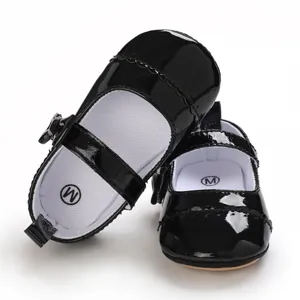 Detail view of black glossy baby Mary Jane shoes with bow decoration and soft sole.