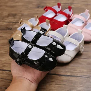 Hand holding a pair of black glossy baby Mary Jane shoes with multiple colors shown